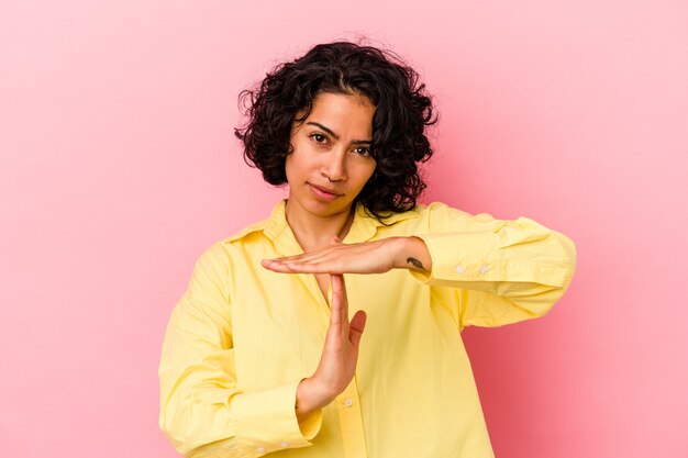 Jovem mulher latina encaracolada isolada em um fundo rosa, mostrando um gesto de tempo limite.