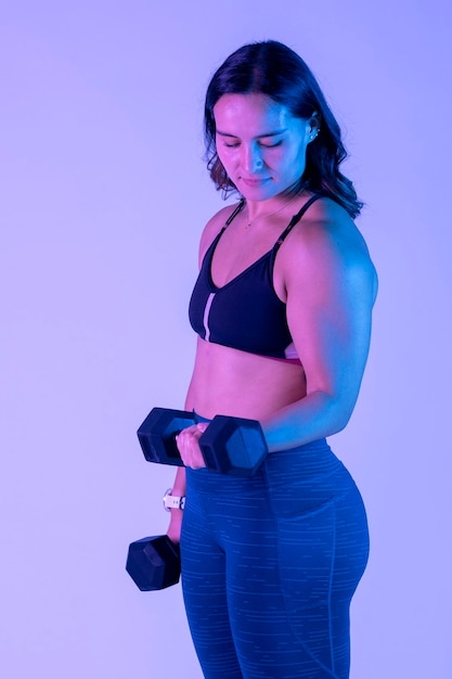 Jovem mulher latina exercitando com halteres em pé no estúdio com cor de fundo