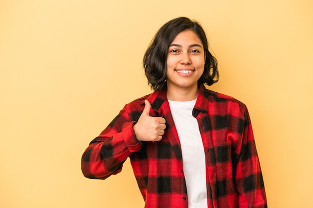 Jovem mulher latina isolada em fundo amarelo sorrindo e levantando o polegar