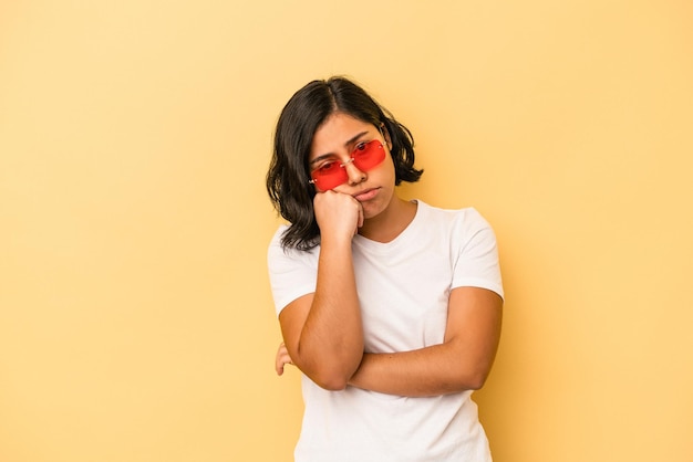 Jovem mulher latina isolada em um fundo amarelo, cansada de uma tarefa repetitiva.