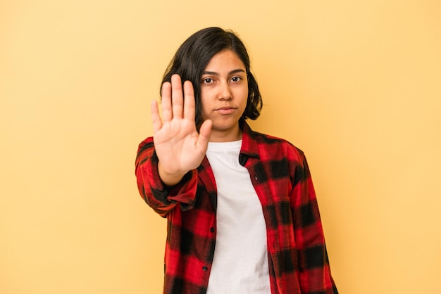 Jovem mulher latina isolada em um fundo amarelo de pé com a mão estendida, mostrando o sinal de stop, impedindo você.