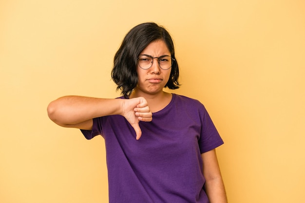 Jovem mulher latina isolada em um fundo amarelo, mostrando o polegar para baixo e expressando antipatia.