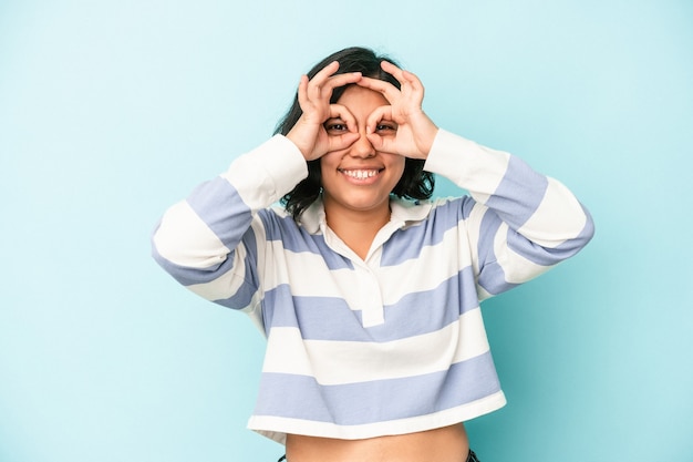 Jovem mulher latina isolada em um fundo azul animado mantendo o gesto ok no olho.