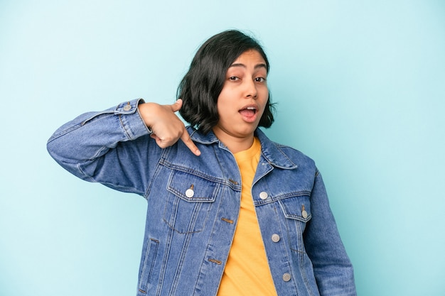 Jovem mulher latina isolada em um fundo azul pessoa apontando com a mão para um espaço de cópia de camisa, orgulhosa e confiante