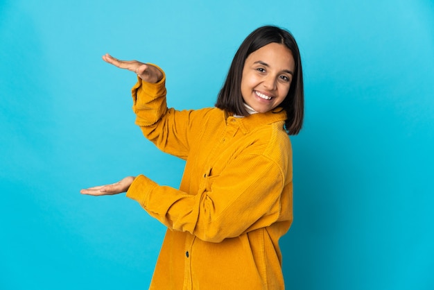 Jovem mulher latina isolada em um fundo azul segurando copyspace para inserir um anúncio