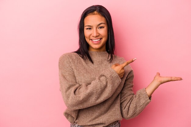 Jovem mulher latina isolada em um fundo rosa animado segurando um espaço de cópia na palma da mão.