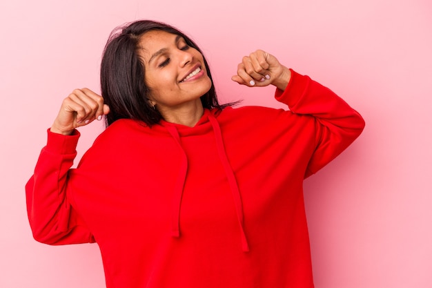 Jovem mulher latina isolada em um fundo rosa, esticando os braços, posição relaxada.