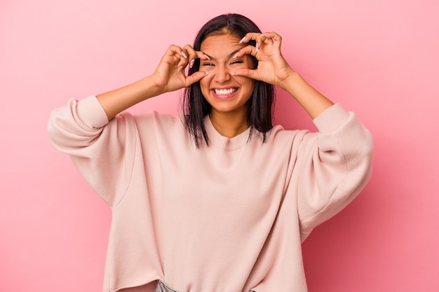 Jovem mulher latina isolada em um fundo rosa, mantendo os olhos abertos para encontrar uma oportunidade de sucesso.