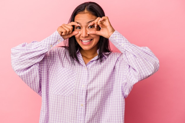 Jovem mulher latina isolada em um fundo rosa, mantendo os olhos abertos para encontrar uma oportunidade de sucesso.