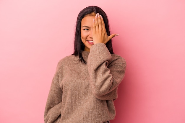 Jovem mulher latina isolada em um fundo rosa se divertindo cobrindo metade do rosto com a palma da mão.