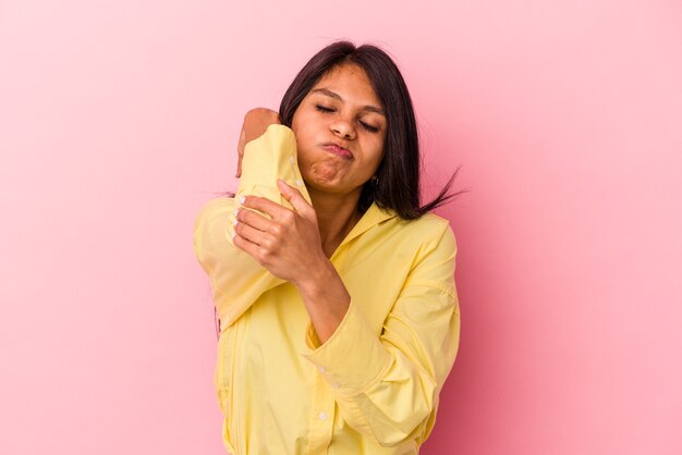 Jovem mulher latina isolada em um fundo rosa, tendo uma dor de garganta devido ao estresse, massageando e tocando com a mão.