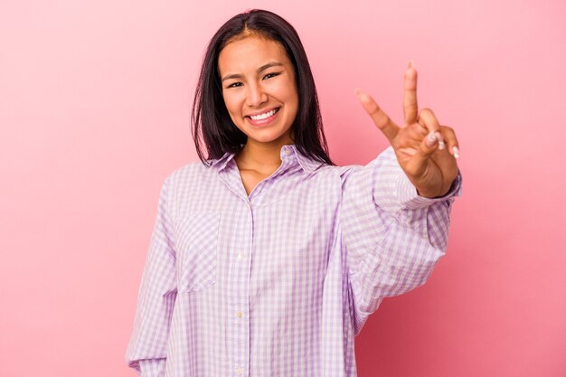 Jovem mulher latina isolada no fundo rosa alegre e despreocupada, mostrando um símbolo de paz com os dedos.