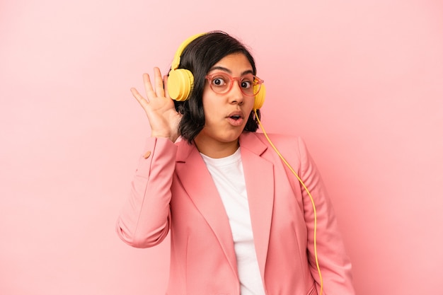 Jovem mulher latina ouvindo música isolada em fundo rosa, tentando ouvir uma fofoca.