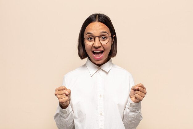 Jovem mulher latina se sentindo chocada, animada e feliz, rindo e comemorando o sucesso, dizendo uau!