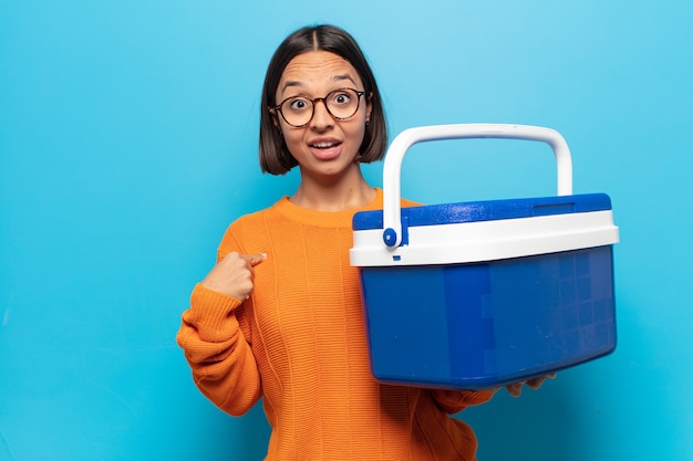 Jovem mulher latina se sentindo feliz, surpresa e orgulhosa, apontando para si mesma com um olhar animado e surpreso