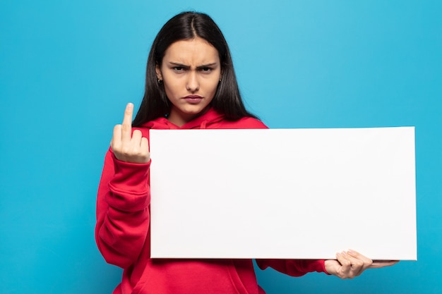 Jovem mulher latina se sentindo irritada, irritada, rebelde e agressiva, sacudindo o dedo do meio e lutando contra