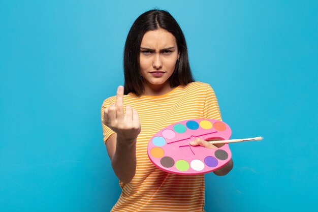 Jovem mulher latina se sentindo irritada, irritada, rebelde e agressiva, sacudindo o dedo do meio e lutando