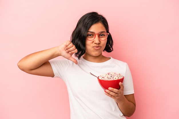 Jovem mulher latina segurando cereais isolados em um fundo rosa se sente orgulhosa e autoconfiante, exemplo a seguir.