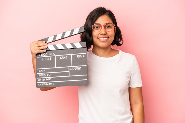 Foto jovem mulher latina segurando claquete isolada no fundo rosa feliz, sorridente e alegre.