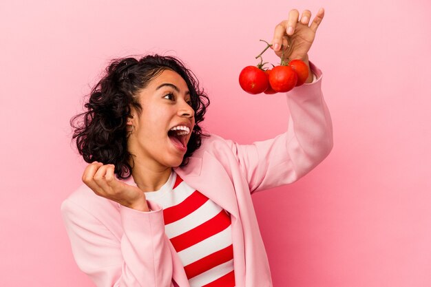 Jovem mulher latina segurando tomates isolados em um fundo rosa