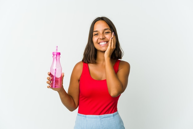 Jovem mulher latina segurando um milkshake isolado no fundo branco mantém o espaço da cópia na palma da mão, mantenha a mão sobre a bochecha. Espantado e encantado.