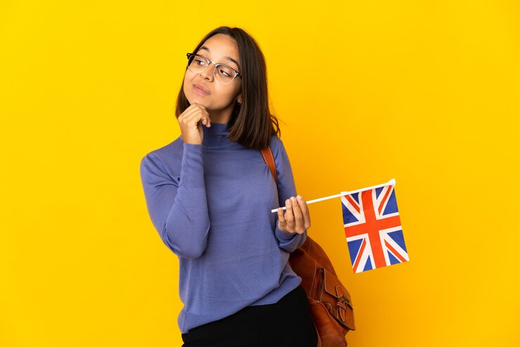 Foto jovem mulher latina segurando uma bandeira do reino unido isolada em um fundo amarelo pensando uma ideia enquanto olha para cima