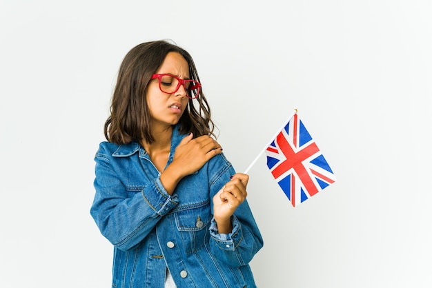 Jovem mulher latina segurando uma bandeira inglesa isolada no branco, tendo uma dor no ombro.