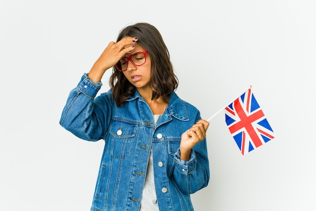 Jovem mulher latina segurando uma bandeira inglesa, isolada no fundo branco, tendo uma dor de cabeça, tocando a frente do rosto.