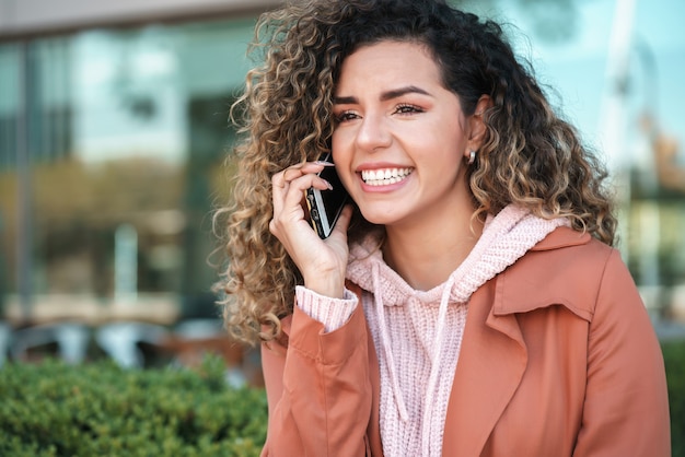 Jovem mulher latina sorrindo enquanto fala ao telefone, ao ar livre na rua. Conceito urbano.