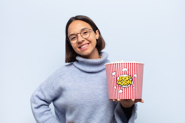 Jovem mulher latina sorrindo feliz com uma mão no quadril e uma atitude confiante, positiva, orgulhosa e amigável