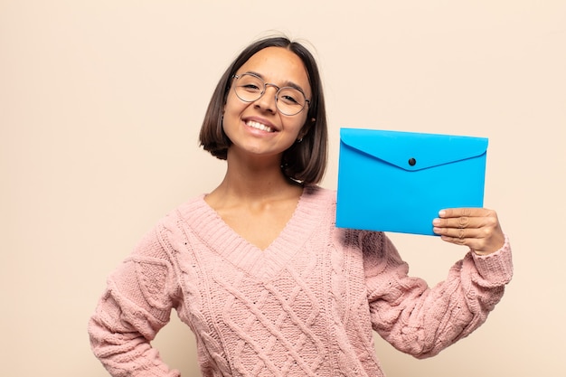 Foto jovem mulher latina sorrindo feliz com uma mão no quadril e uma atitude confiante, positiva, orgulhosa e amigável