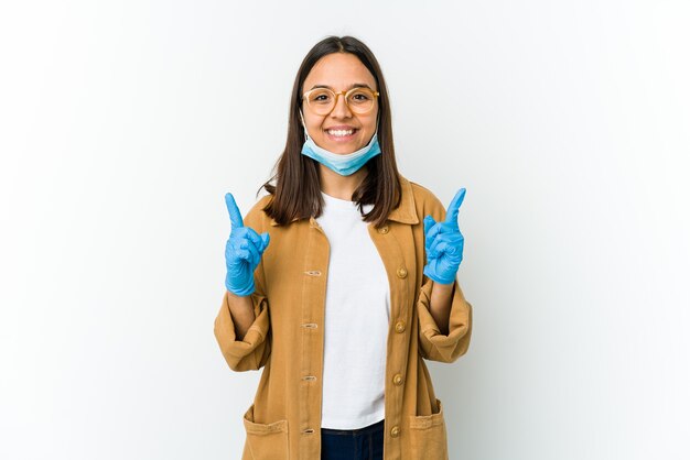 Jovem mulher latina usando uma máscara para se proteger de cobiça indica com os dois dedos anteriores mostrando um espaço em branco.