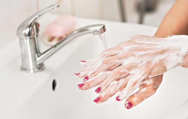 Jovem mulher lavando as mãos sob a torneira de água com sabão. Detalhe na pele coberta de espuma. Conceito de higiene pessoal - prevenção de surtos de coronavírus covid 19