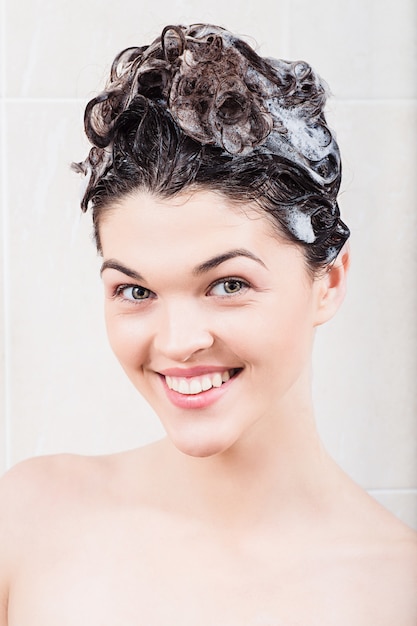 Jovem mulher lavando o cabelo com o shampoo no chuveiro