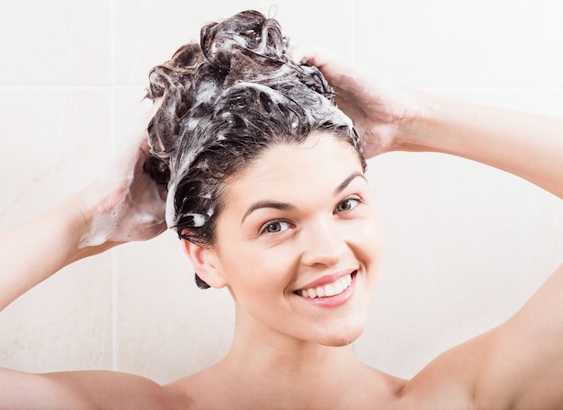 Jovem mulher lavando o cabelo com o shampoo no chuveiro