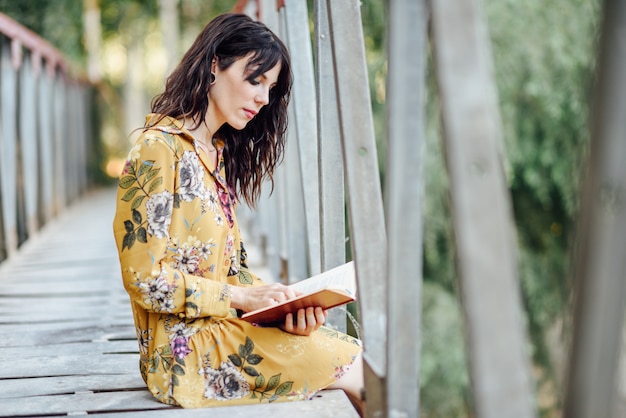 Jovem mulher lendo um livro em uma ponte rural.