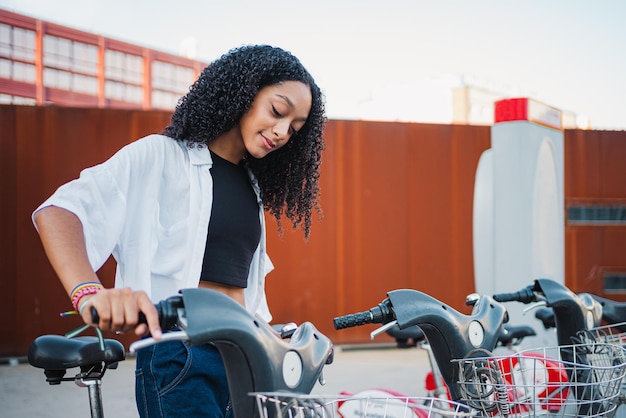 Jovem mulher liberando uma bicicleta da estação de bicicletas na cidade