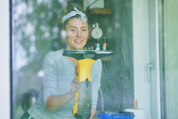 Jovem mulher limpando a janela na cozinha