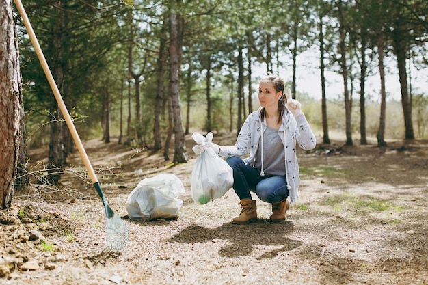 Foto jovem mulher limpando o lixo segurando sacos de lixo e apontando o dedo indicador para cima no parque. problema de poluição ambiental