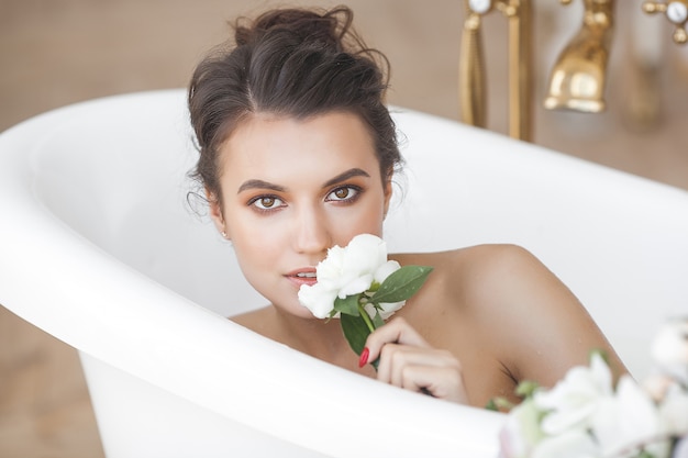 Jovem mulher linda tomando banho com flores e leite