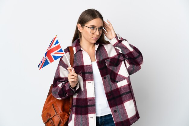 Jovem mulher lituana segurando uma bandeira do Reino Unido, isolada na parede branca, tendo dúvidas e pensando