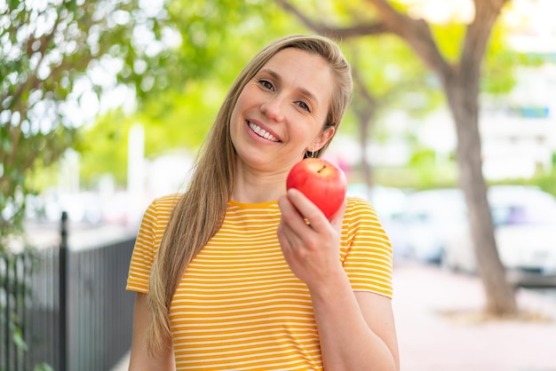 Jovem mulher loira ao ar livre com uma maçã e feliz