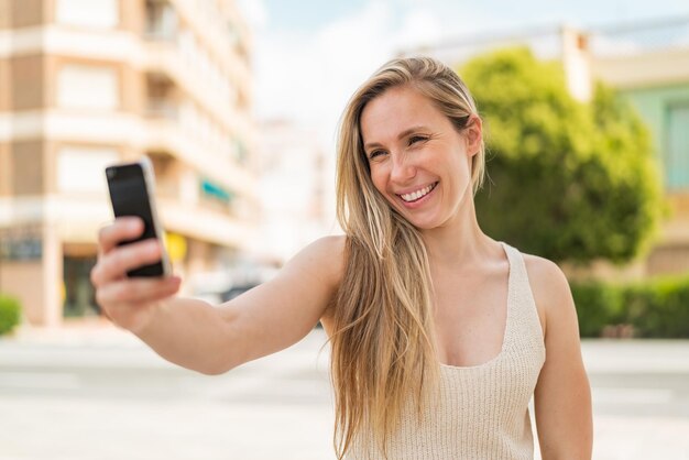 Jovem mulher loira ao ar livre fazendo uma selfie