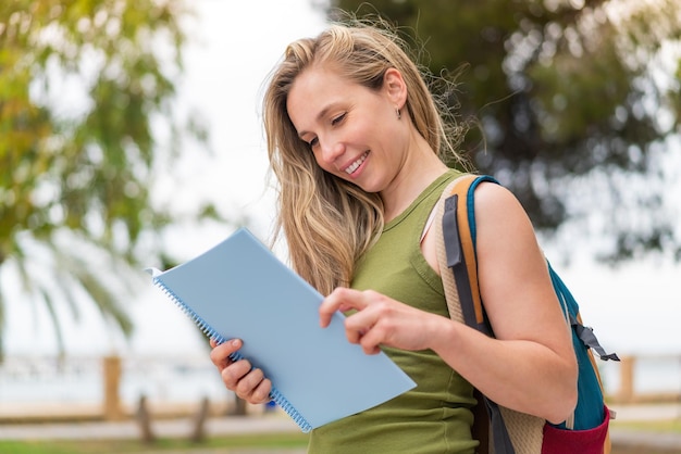 Jovem mulher loira ao ar livre segurando um caderno