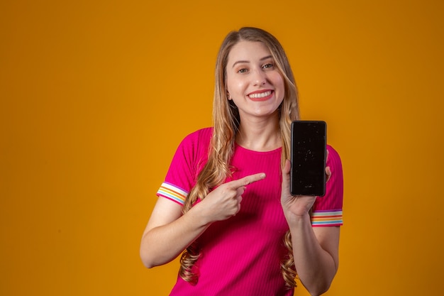 Jovem mulher loira apontando para o celular.