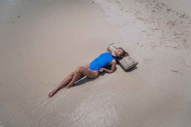 Jovem mulher loira atraente em um maiô azul deitado na praia. Conceito de férias de verão