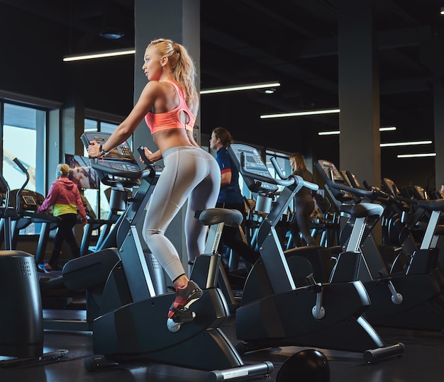 Jovem mulher loira bonita no treinamento esportivo em uma bicicleta ergométrica em um moderno centro de fitness.