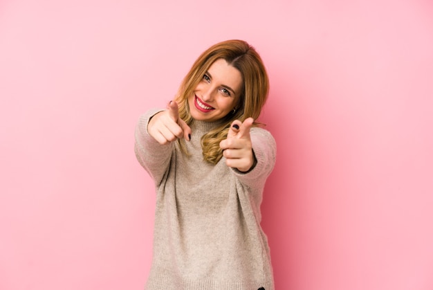 Jovem mulher loira bonita vestindo um suéter isolado sorrisos alegres apontando para a frente.