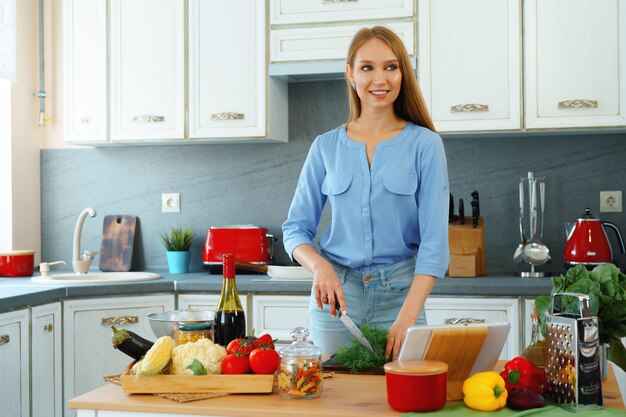 Jovem mulher loira caucasiana cortando vegetais para salada na cozinha