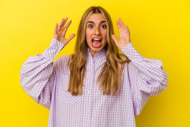 Jovem mulher loira caucasiana isolada em fundo amarelo, comemorando uma vitória ou sucesso, ele fica surpreso e chocado.